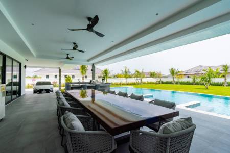 Covered outdoor dining area by a swimming pool with garden view