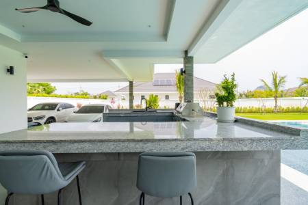 Outdoor kitchen and seating area with pool and garden view