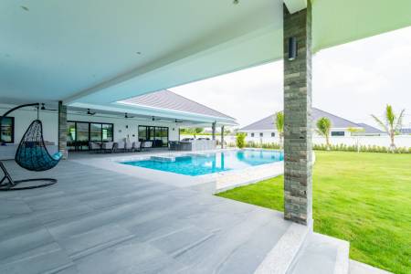 Outdoor pool area with covered patio and surrounding lawn