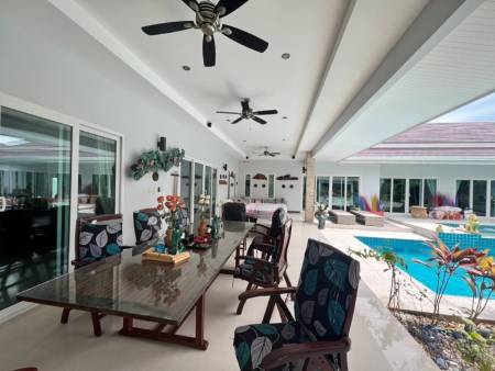 Covered patio dining area next to a swimming pool and garden